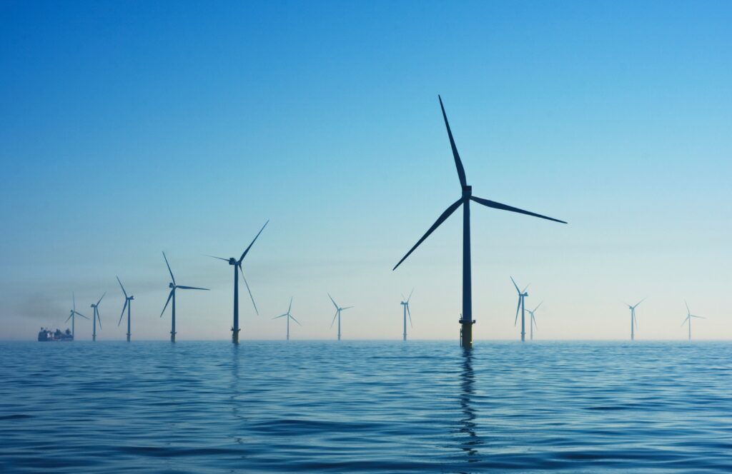 A row of offshore wind turbines extending across calm ocean waters under a clear blue sky – EMFSA November 2025 Newsletter Updates.