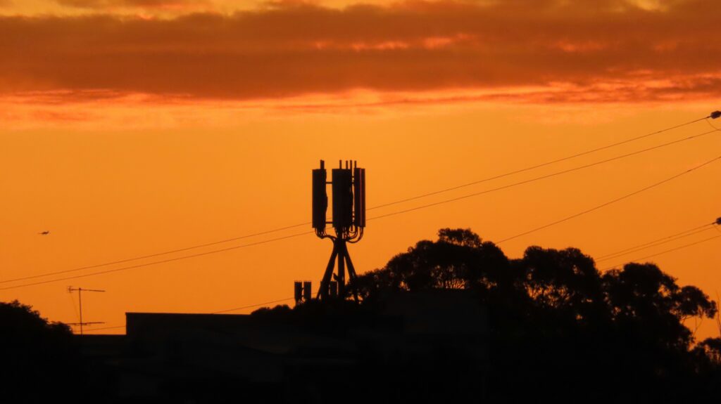 Cell tower silhouetted at sunset representing mobile network exposure that varies with human activity patterns across European countries